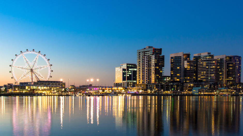 Evening citylights reflecting in water with an observation wheel sparkling in the distance in Melbourne