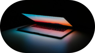 A laptop with a glowing screen displaying a sunset-like gradient, set against a dark background