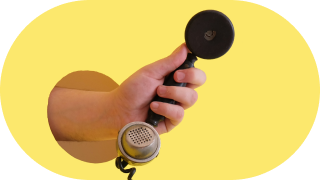A hand holding an old-fashioned telephone receiver against a yellow background