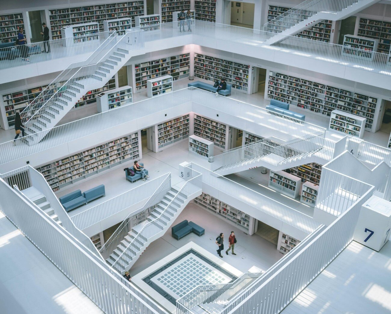 A bright, modern multi-level library with white walls, open staircases, and bookshelves lining each floor